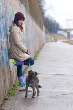 güzel genç kız köpekle bulutlu kış gününde duvara yaslanmış
