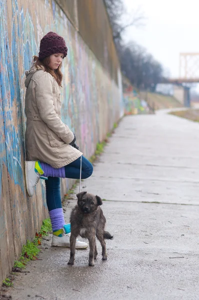 Гарненька дівчина-підліток з собакою спирається на стіну в похмурий зимовий день — стокове фото