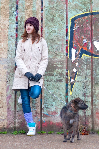 Bastante adolescente con perro apoyado contra la pared en el día nublado de invierno —  Fotos de Stock