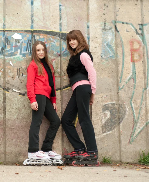 Dos chicas adolescentes bastante sonrientes en patines de pie al aire libre junto a c — Foto de Stock