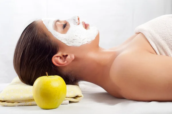 Hermosa mujer joven acostada en la mesa de masaje con máscara facial natural en su cara —  Fotos de Stock
