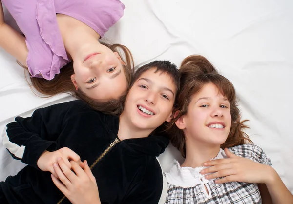 Two smiling teenage girls and one smiling teenage boy resting on bed — Stock Photo, Image