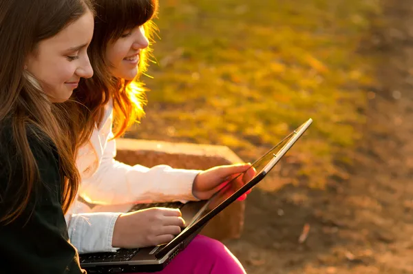 Two beautiful teenage girls having fun with notebook in the park on sunny spring day — Stock Photo, Image