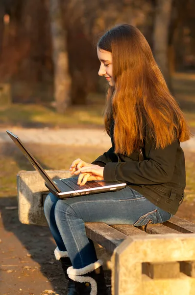 Vrij tienermeisje te typen op laptop in het park op zonnige lentedag — Stockfoto