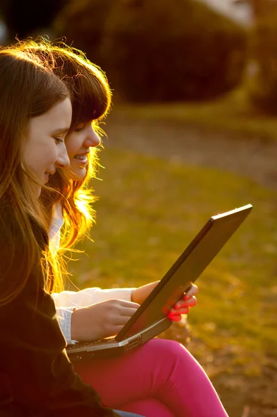 Dvě krásné mladé dívky baví s notebookem v parku na slunný jarní den — Stock fotografie