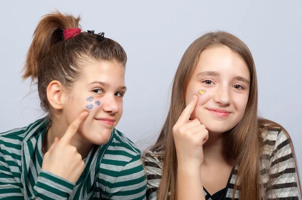 Duas belas meninas adolescentes sorridentes mostrando corações em seus rostos — Fotografia de Stock