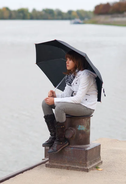 Hermosa adolescente sentada en la columna del muelle en el día nublado de otoño —  Fotos de Stock