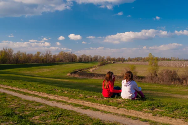 Two teenage girls sitting in the grass and talking on beautiful sunny spring day — Stock Photo, Image