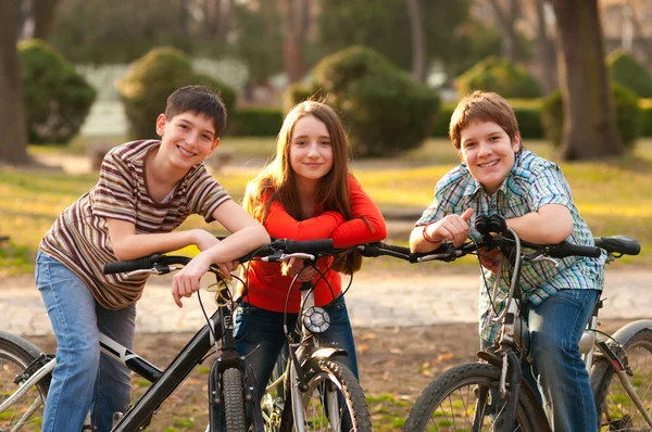Zwei lächelnde Teenager-Jungen und ein Teenager-Mädchen haben Spaß auf Fahrrädern im Park — Stockfoto