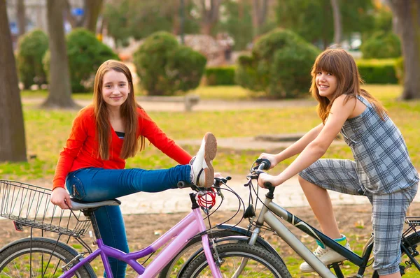 Duas meninas adolescentes bonitas se divertindo nas bicicletas no parque no belo dia de primavera — Fotografia de Stock