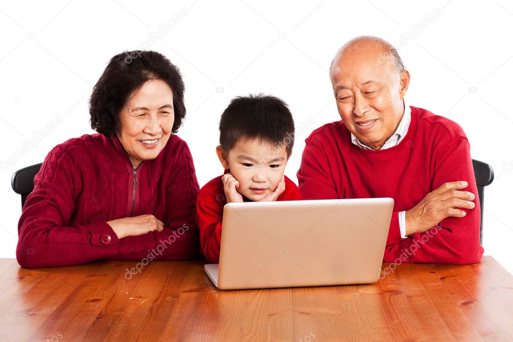 Senior Asian grandparents using computer with their grandson