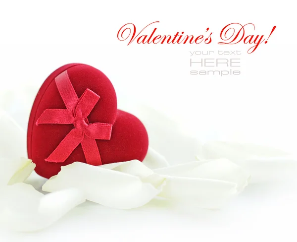 Caja de regalo en forma de corazón de terciopelo rojo en pétalos blancos en una espalda blanca — Foto de Stock