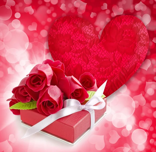 Pequeno presente vermelho com rosas no fundo coração vermelho — Fotografia de Stock