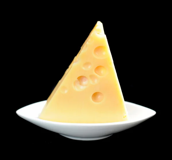 Pedaço de queijo em um prato isolado em um fundo preto — Fotografia de Stock