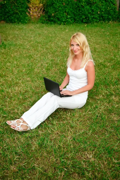 Молода красива жінка працює з ноутбуком у зеленій траві — стокове фото