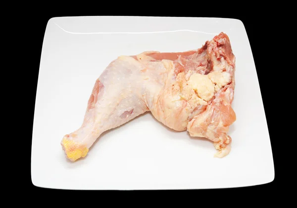 Pollo fresco pierna entera en un plato blanco sobre un fondo negro —  Fotos de Stock
