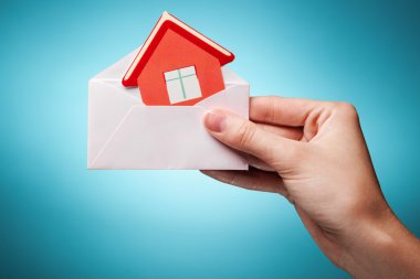 Woman's hand holding an envelope with a sign of the house agains clipart