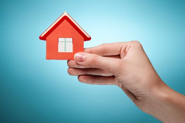 Woman's hand holding sign of the house. Against blue background clipart