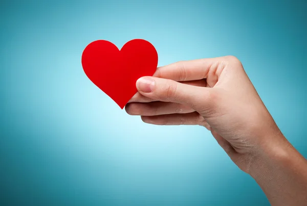 Kvinnans hand innehav symbol - rött hjärta. Mot blå bakgrund — Stockfoto