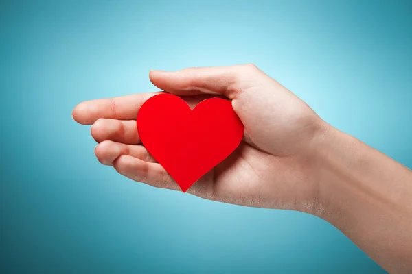 Woman's hand holding symbol - red heart. Against blue background — Stock Photo, Image