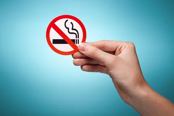 stock image Woman's hand holding a symbol - no smoking. Against blue backgro