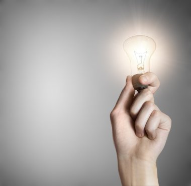 Glowing lightbulb in a hand on gray background with copyspace clipart