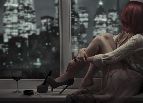 Одна красивая женщина сидит на окне и смотрит на ночной цит — стоковое фото
