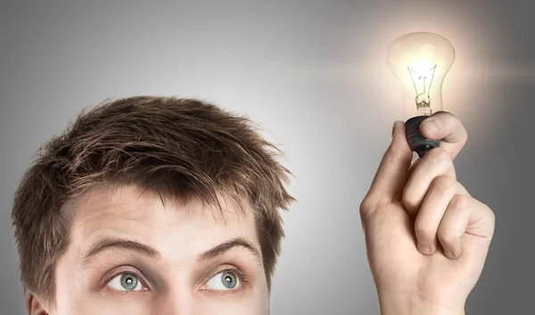 Funny young man with light bulb, on gray background — Stock Photo, Image