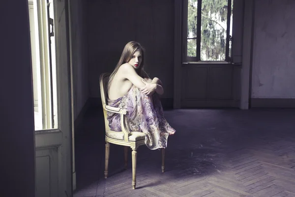 아름 다운 여자는 빈 룸에 오래 된의 자에 앉아 — 스톡 사진