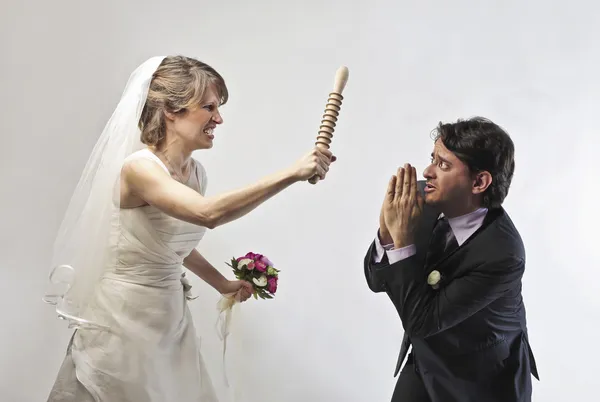 Angry bride waving threateningly a rolling pin against her husband — Stock Photo, Image
