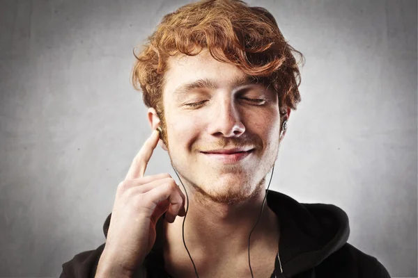 Smiling young man listening with pleasure to music — Stock Photo, Image