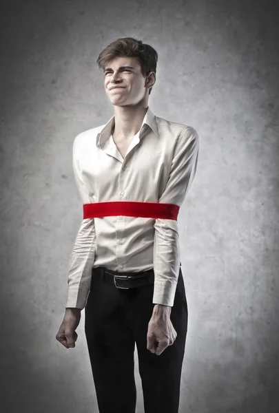 Frustrerad ung affärsman med ett rött bandage som blockerar hans rörelser — Stockfoto