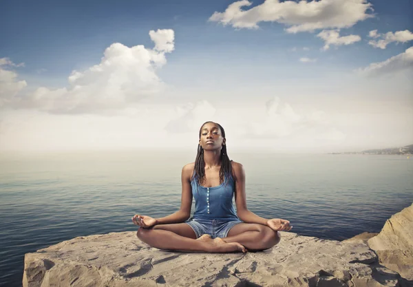 Gyönyörű afrikai nő ül egy csúcs a tenger fölött, és meditál — Stock Fotó