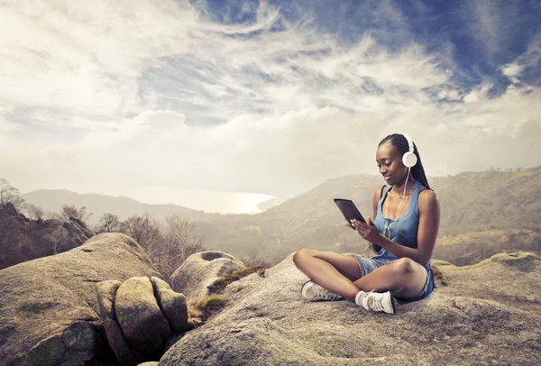 Sorrindo mulher africana sentado em uma rocha e usando um tablet pc — Fotografia de Stock