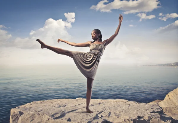 Beautiful elegant african woman dancing on a peak over the sea — Stock Photo, Image
