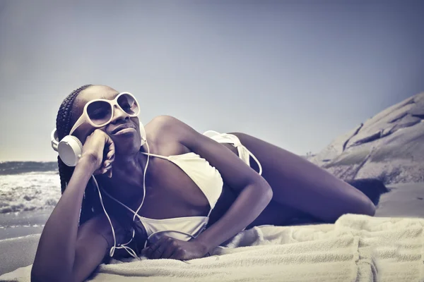 Beautiful african woman lying on a beach and listening to music — Stock Photo, Image