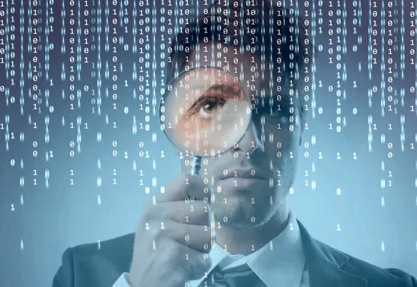 Young businessman observing a binary code on a screen through a magnifying glass — Stock Photo, Image