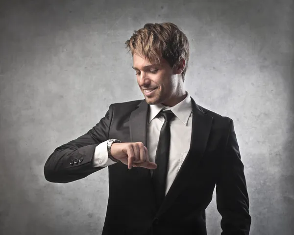 Улыбающийся молодой бизнесмен смотрит на свои наручные часы — стоковое фото