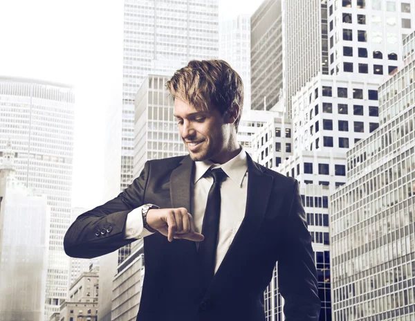 Glimlachend jonge ondernemer op zoek naar zijn horloge met stadsgezicht in de achtergrond — Stockfoto