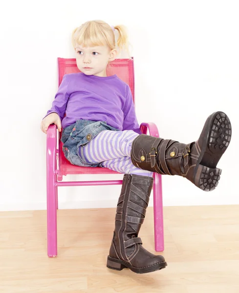 Little girl wearing boots sitting on chair — Zdjęcie stockowe