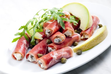 Parma ham rolls filled with cream cheese, Galia melon and capers clipart