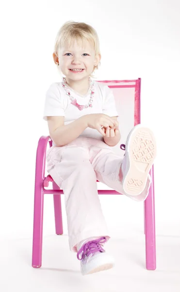 Маленька дівчинка в намисті сидить на стільці — стокове фото