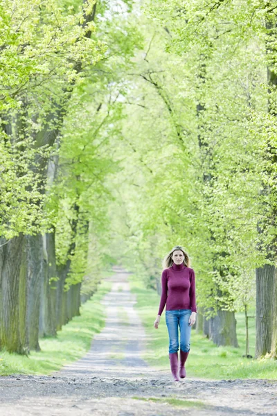 Mujer con botas de goma caminando en el callejón de primavera —  Fotos de Stock