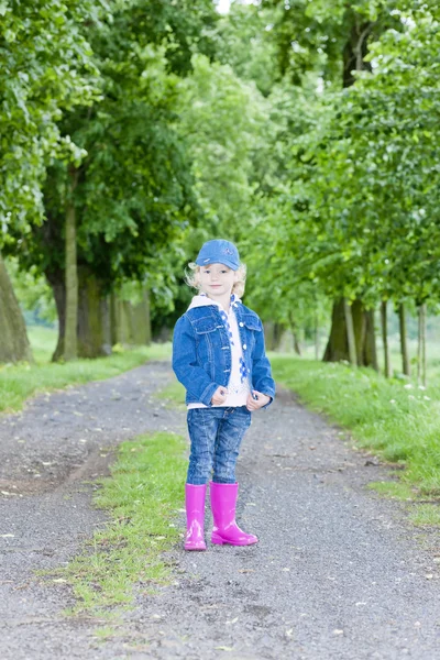 Little girl wearing rubber boots in spring alley — Stock Photo, Image