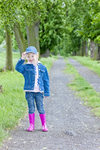 Little girl wearing rubber boots in spring alley — Stock Photo, Image