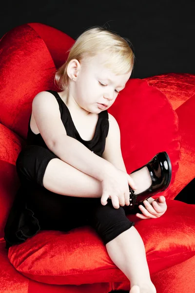 Маленька дівчинка з чорним взуттям сидить на червоному кріслі — стокове фото