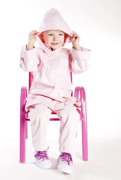 Kleines Mädchen im Regenmantel sitzt auf Stuhl — Stockfoto