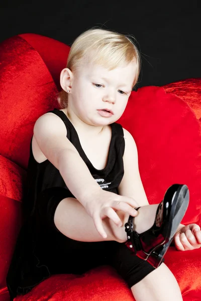 Little girl with black shoes sitting on red armchair