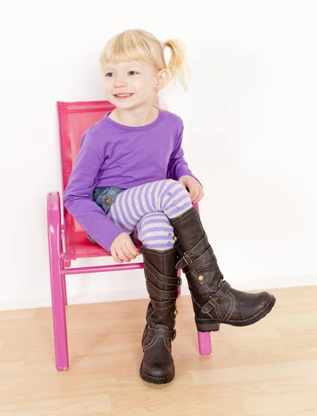Liten flicka klädd i stövlar sitter på stol — Stockfoto