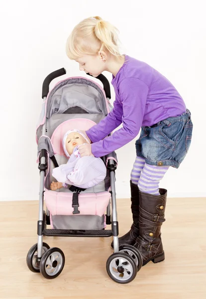 Liten flicka som leker med en docka och en barnvagn — Stockfoto